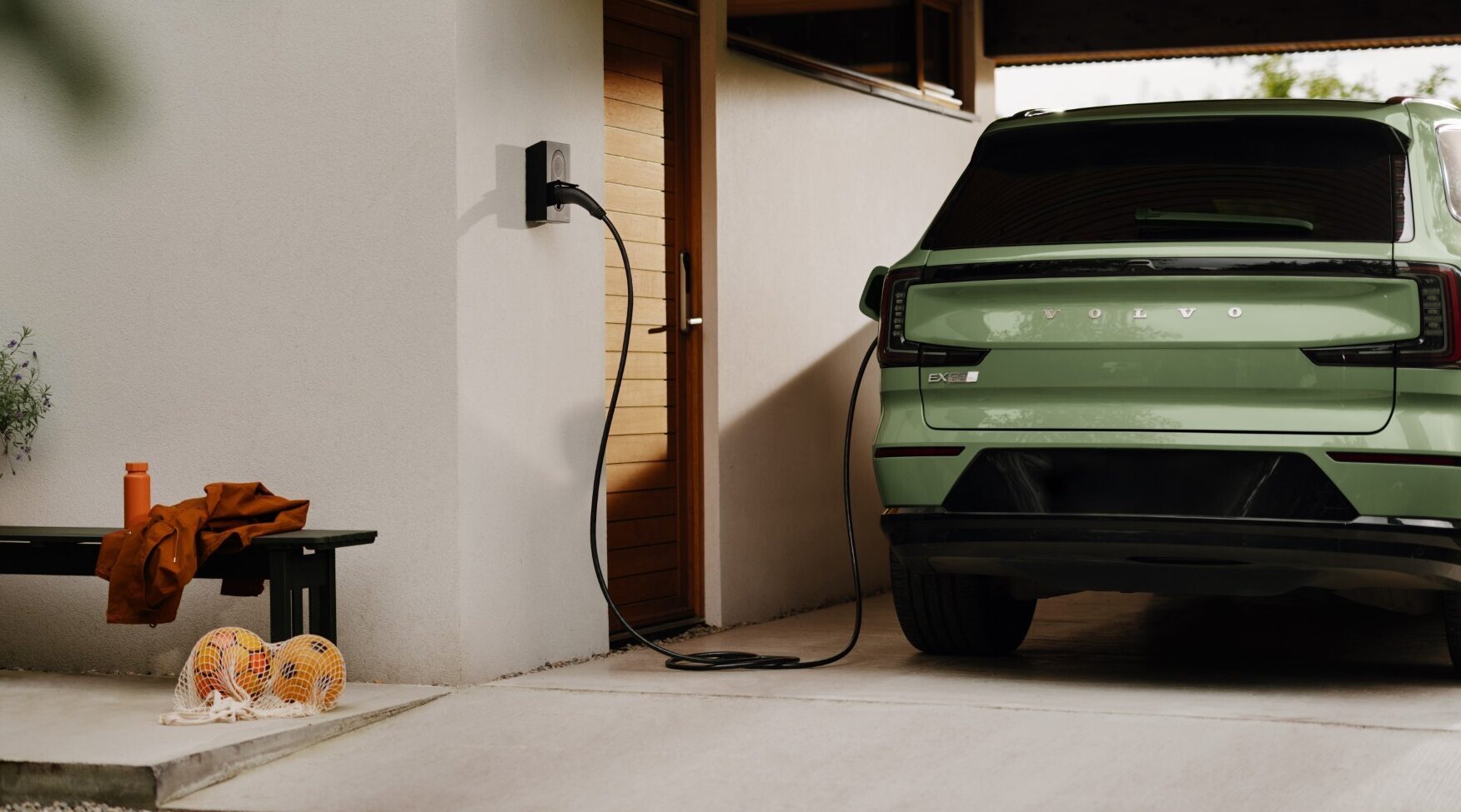 Elbil koblet til lader utenfor en bolig, med ladekabel tilkoblet veggmontert ladepunkt.