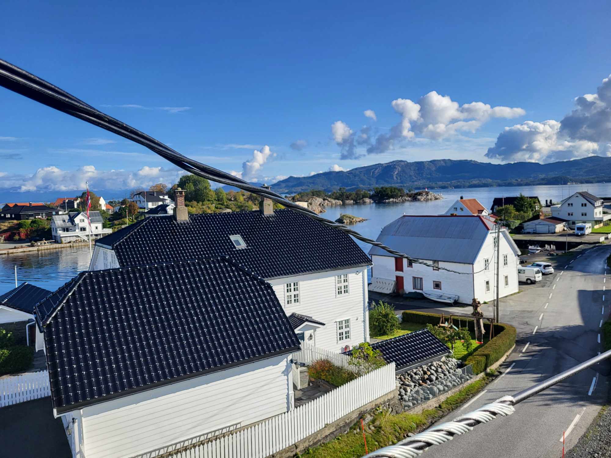 Bustadhus ved sjøen med straumlinjer i forgrunnen og fjell i bakgrunnen.