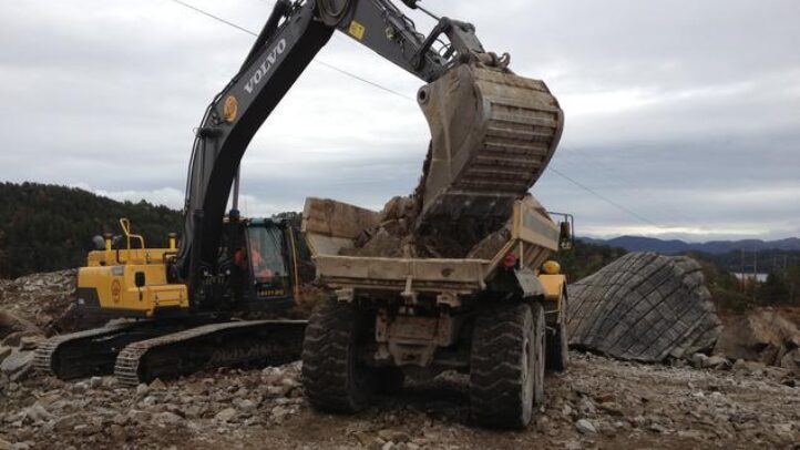 Gravemaskin lastar stein i dumper på anleggsområde.